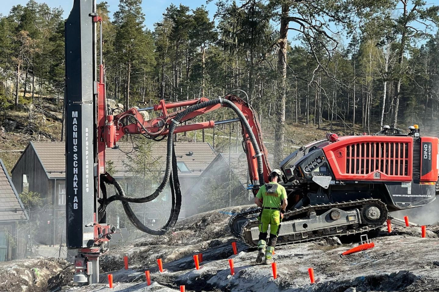 En berghäll med många så borrhål, förberedd för sprängning. Människa som kontrollerar. I bakgrunden en stor maskin.