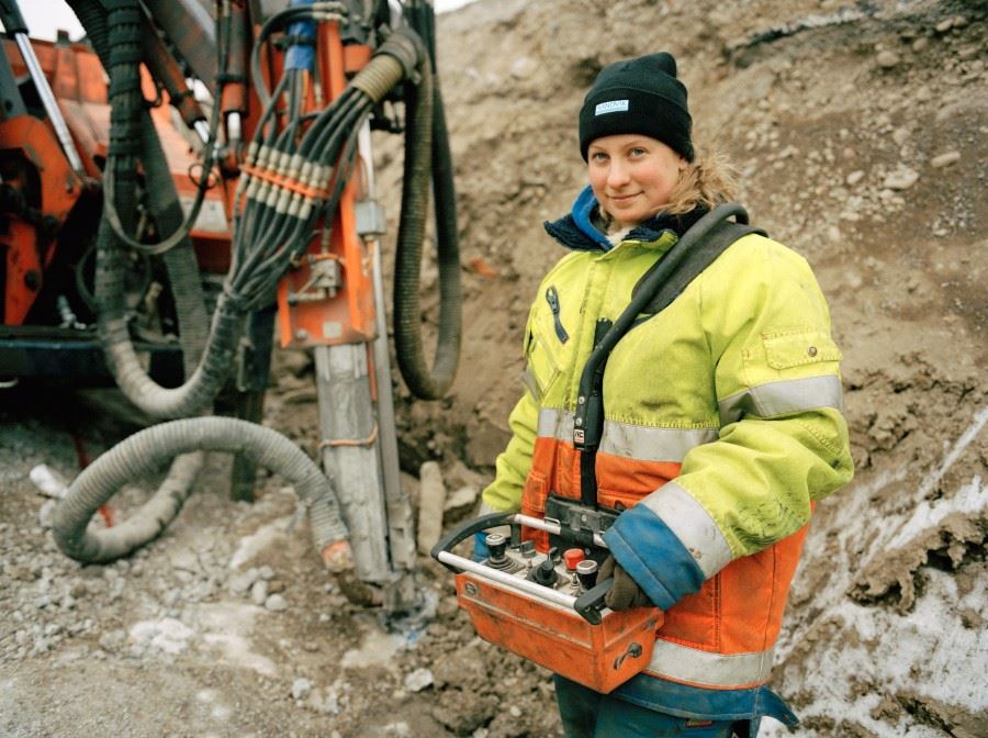 Kvinna utomhus i arbetskläder vid bygge.