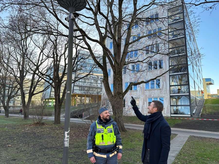 En ordningsvakt och en person står vid en stolpe som har en kamera installerad på sig.