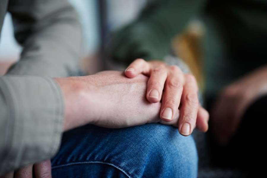En hand läggs på en persons knä. Bilden illustrerar ett tröstande samtal.