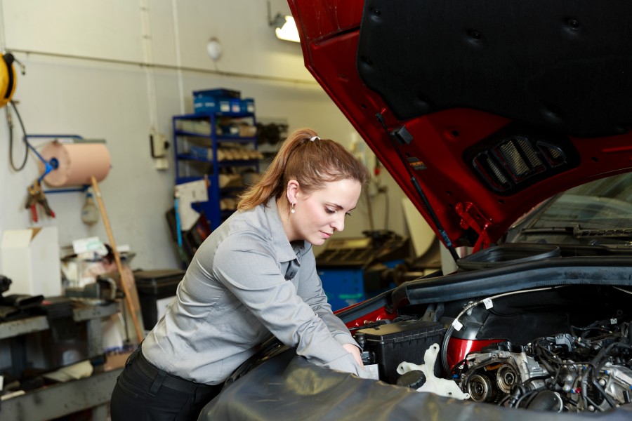 Bilden visar en bil med öppen motorhuv och en mekaniker som arbetar.