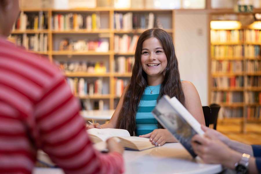 Ung tjej sitter på biblioteket med en bok i handen