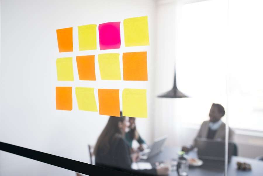 Post-itlappar på en glasvägg - personer runt ett bord syns i bakgrunden