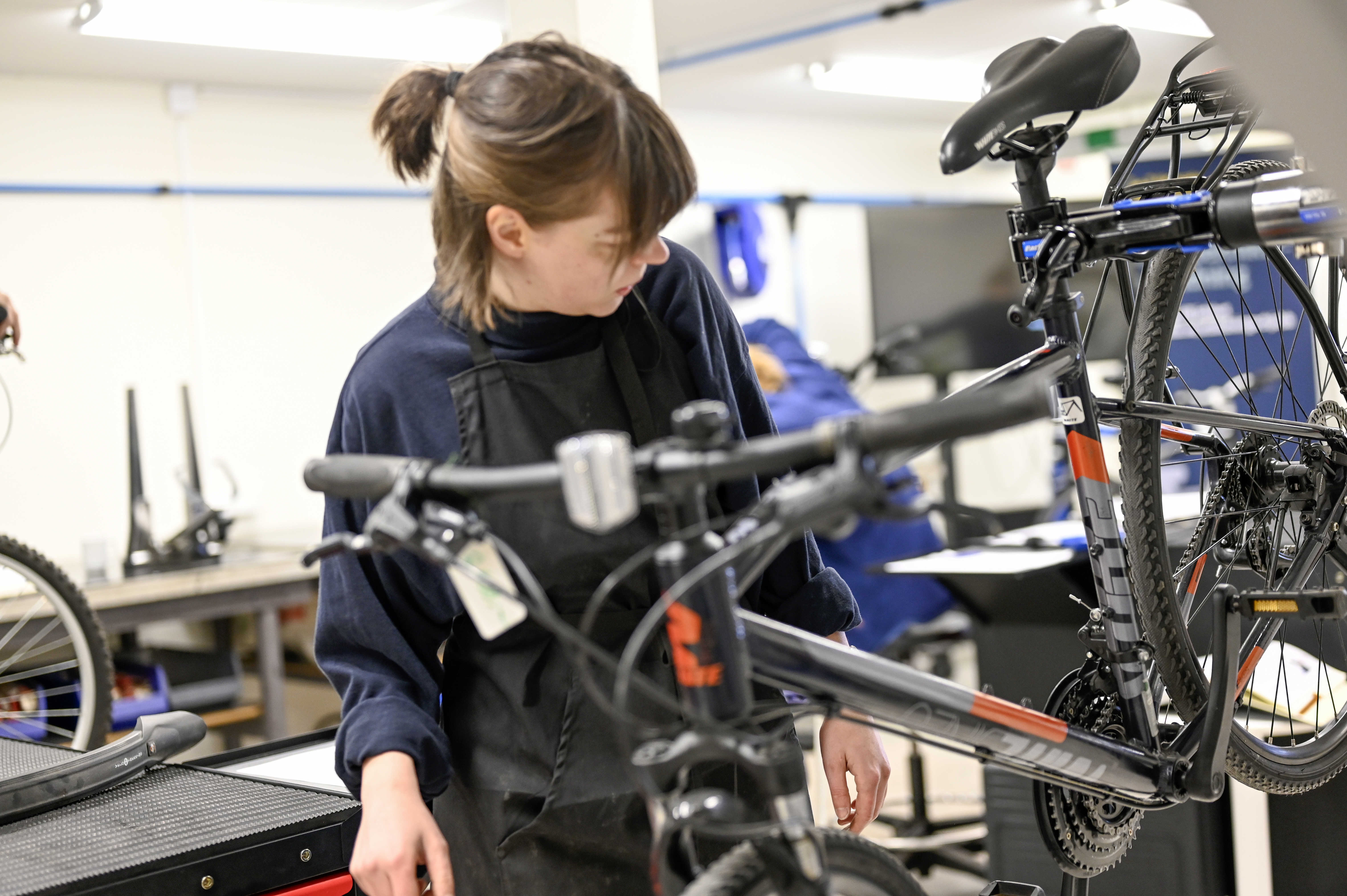 Interiör cykelverkstad, närbild på cykel och en kvinna som lagar den